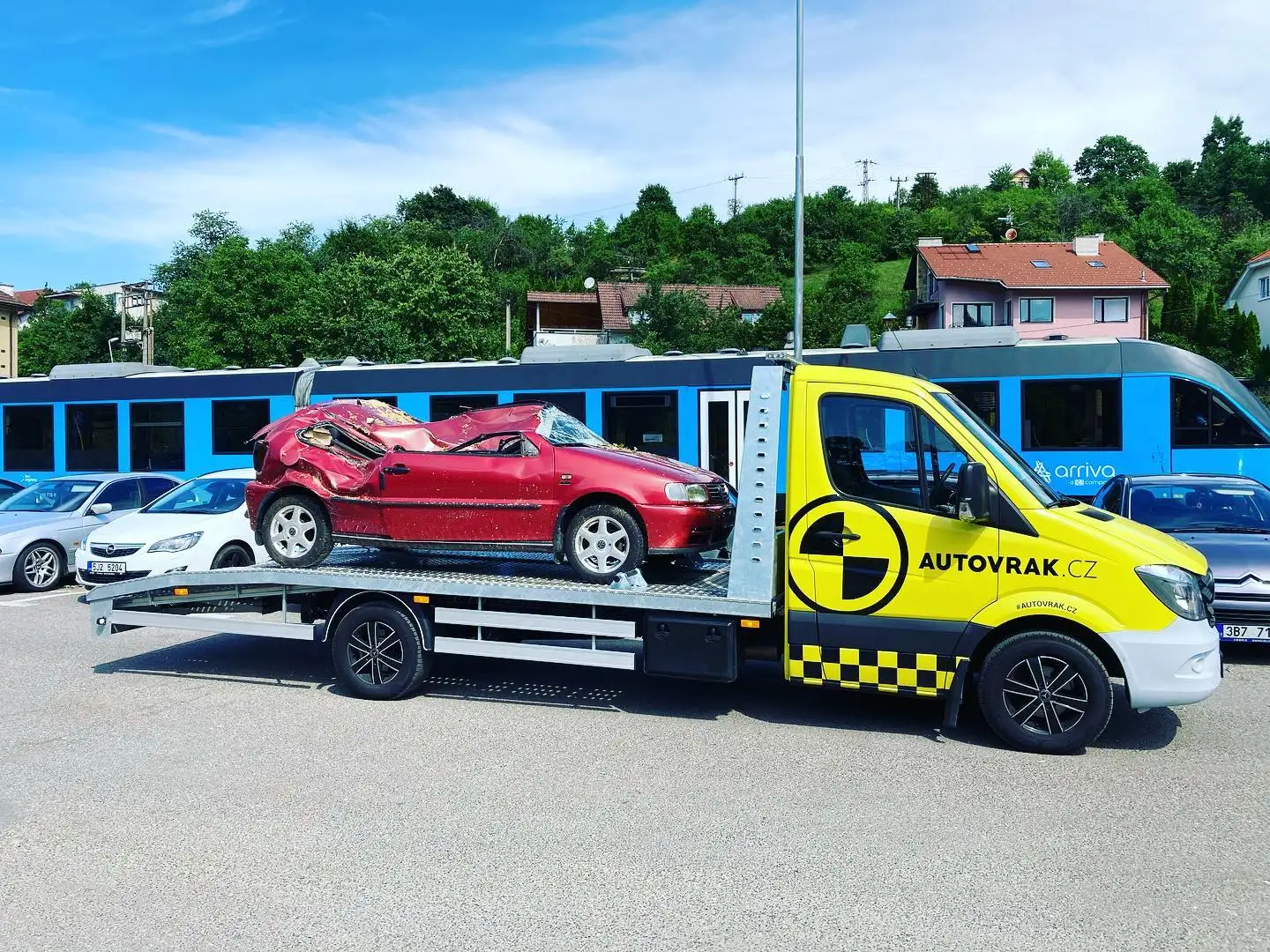 Odtahový vůz Autovrak.cz s naloženým havarovaným autem v ulici města